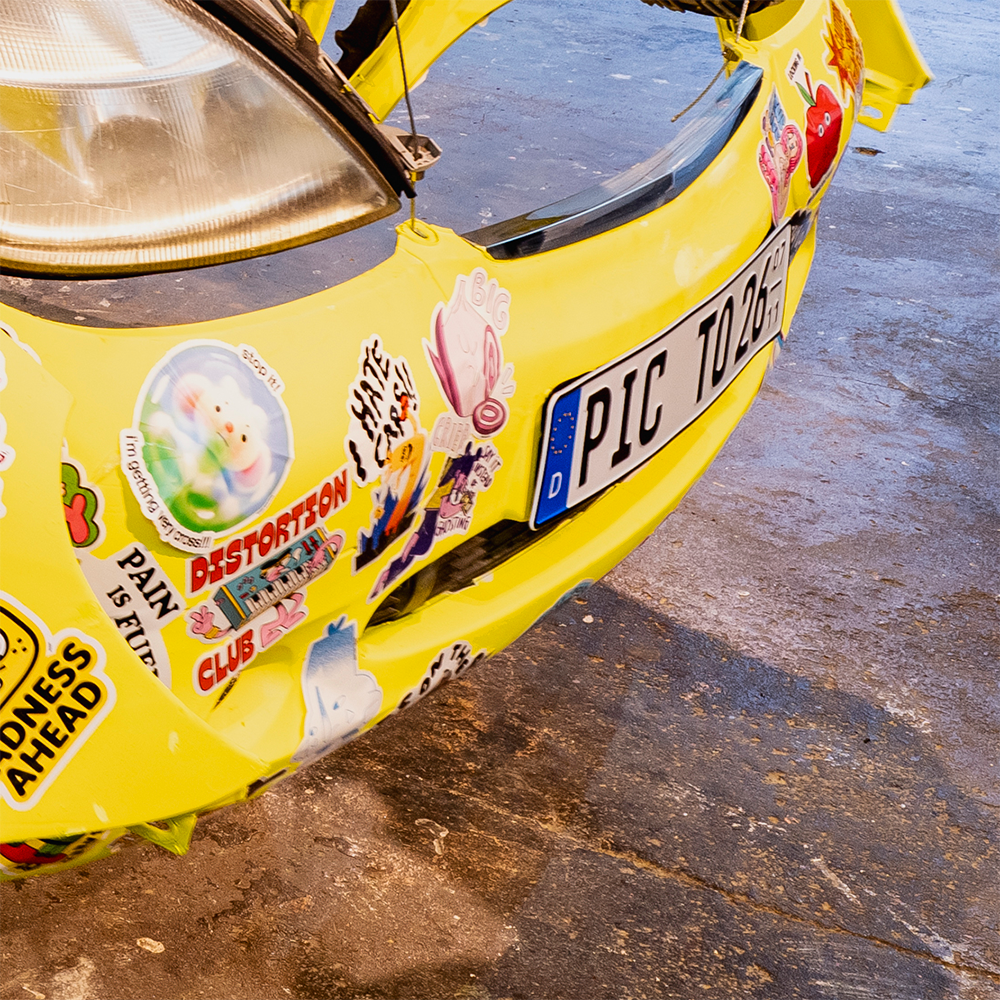 Yellow Mercedes body covered in bumper stickers in various shapes and sizes, with a german licence plate.