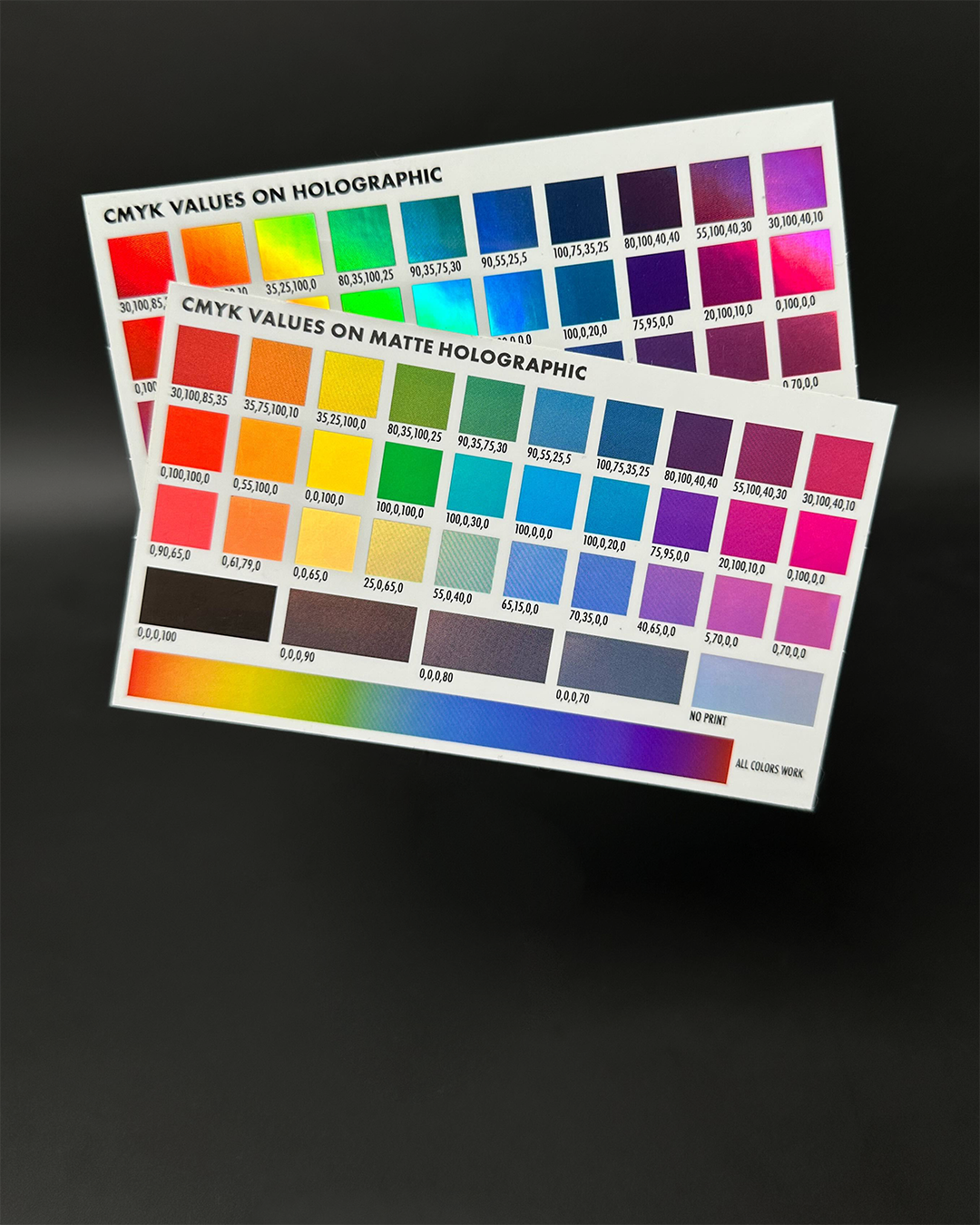 Two printed charts displaying CMYK values on holographic and matte holographic backgrounds, featuring a range of vibrant colors.