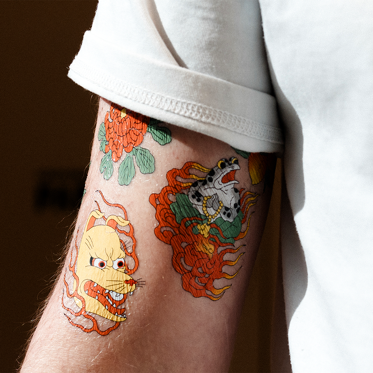 Close-up of an upper arm with colorful temporary tattoos featuring bold, traditional-style designs, partially covered by a rolled-up sleeve.
