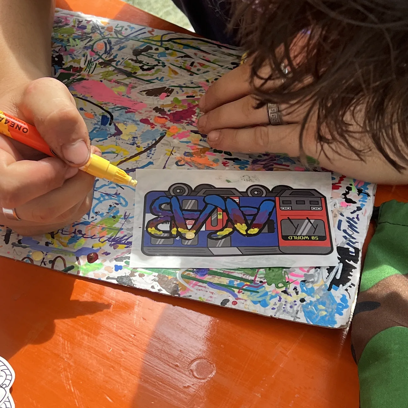 Hand coloring an S8 World train label with a yellow paint marker at the Brainfart x StickerApp workshop
