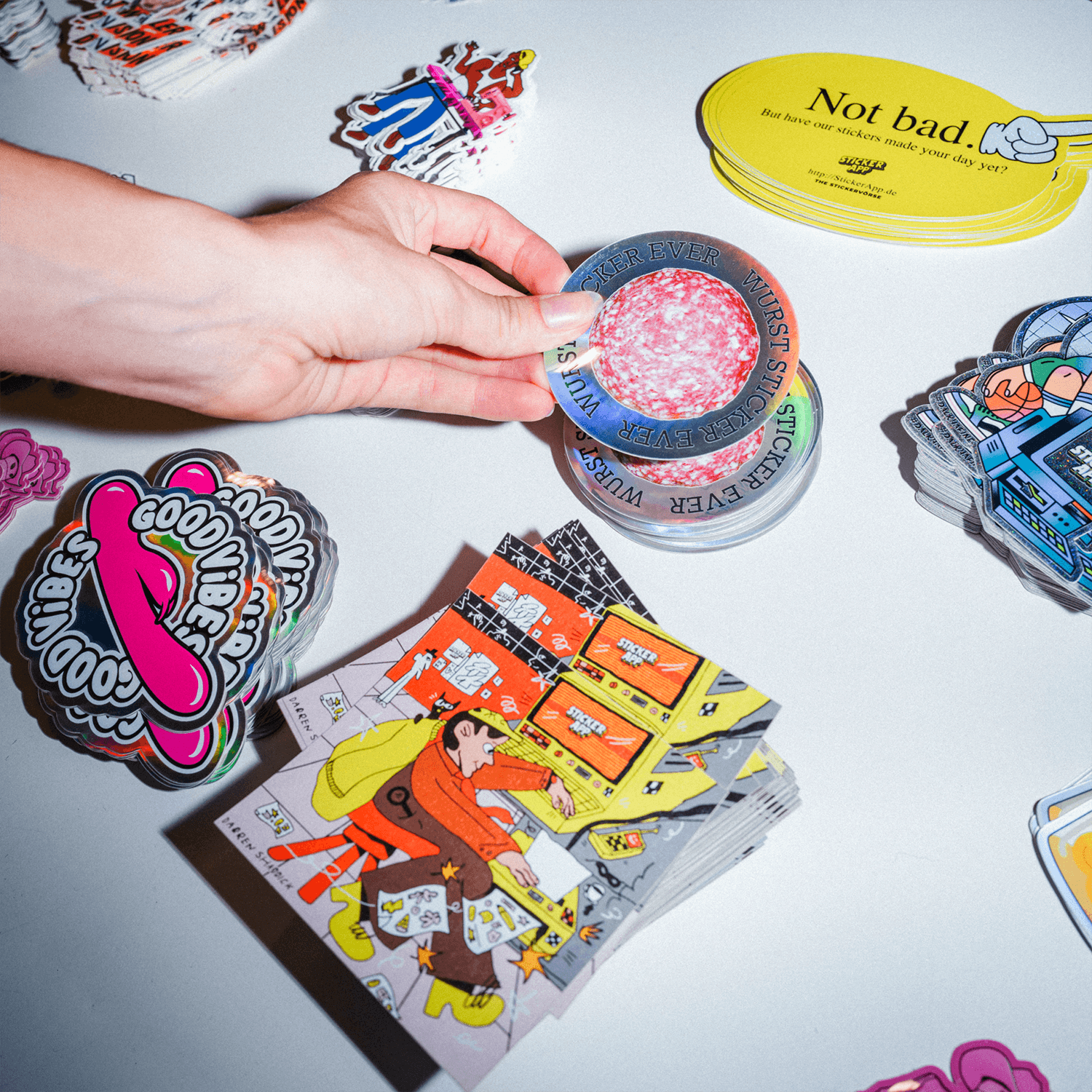 A hand holding a round sticker above various colorful stickers in different sticker materials