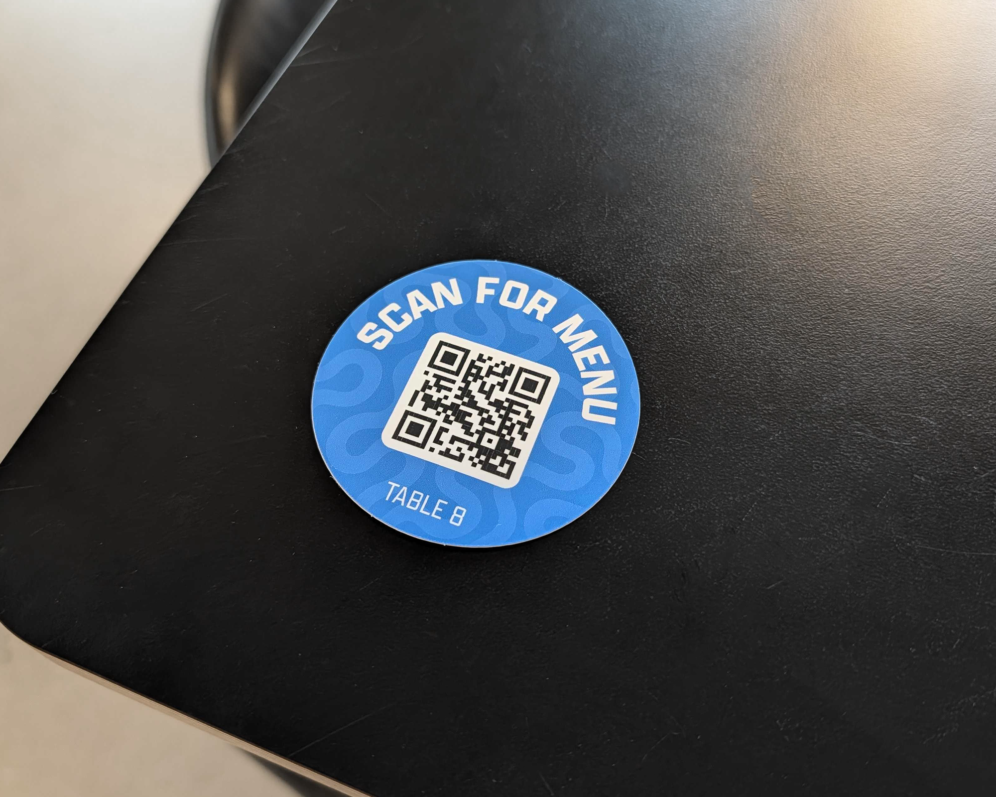 Blue "Scan for menu" QR code sticker for table 8 on a black table