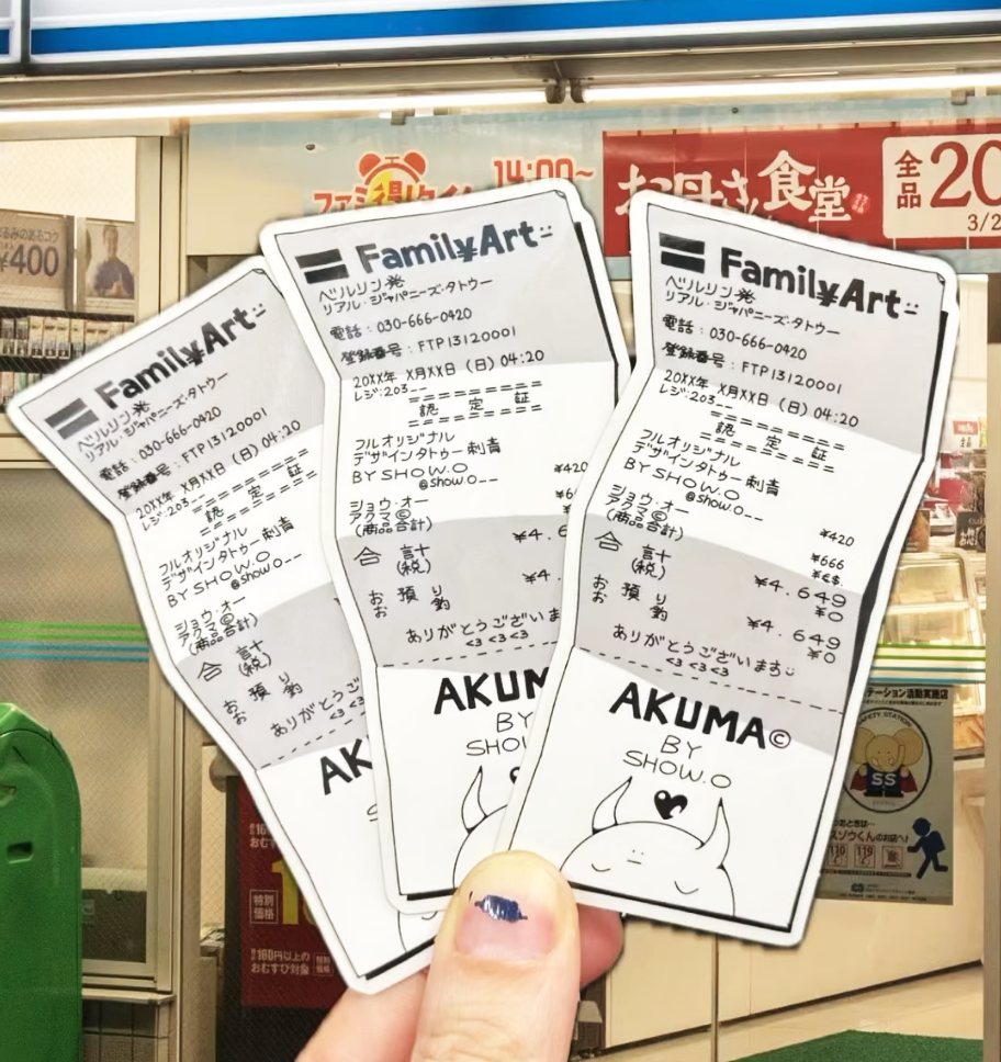 Hand holding three concert tickets with Japanese text, titled "AKUMA by SHOW," in front of a convenience store entrance.